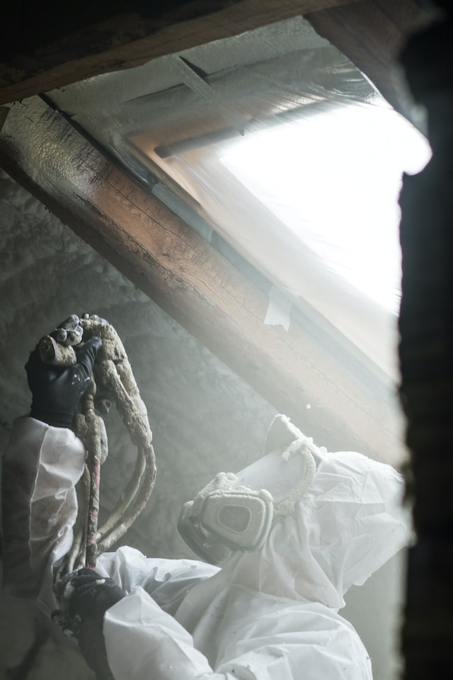 Technician with protective gear applying spray foam insulation in an attic.